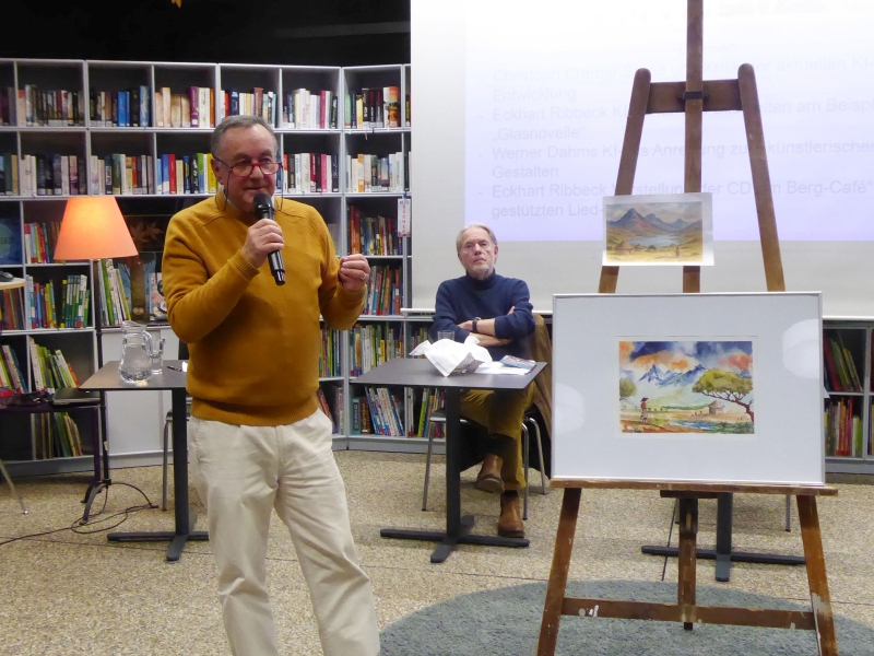 Werner Dahms vor seinem Aquarell „Lesotho“, darüber auf der Staffelei das KI-generierte ausgedruckte Bild. Im Hintergrund Eckhart Ribbeck