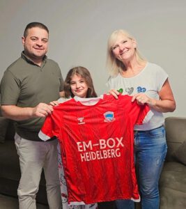 v.l.: Serbest Sindi, Tochter Barin und Redaktionsmitglied Andrea Schliwa zeigen stolz das Vereins-Trikot des SZ Zakho Foto: zg