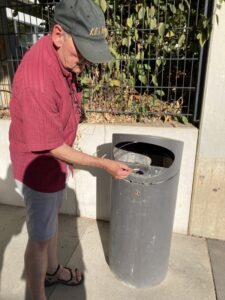 Heinrich Schlosser demonstriert, wie man seine Zigaretten-Kippe nach dem Ausdrücken am Deckelrand des Mülleimers in der kleinen Öffnung ordentlich entsorgt. Dieser „Aschenbecher“ ist im Inneren getrennt vom Rest des Mülls. Foto: Weinmann-Abel